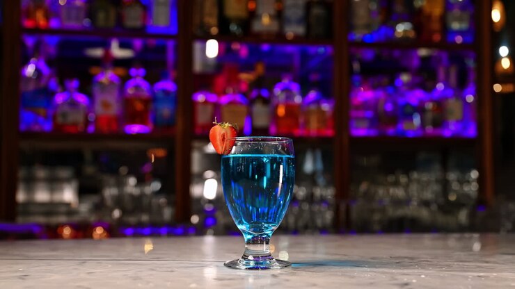 Cocktail blu con fetta di fragola in un bar moderno. Cocktail blu rinfrescante guarnito con fragola sul bancone del bar illuminato da luci al neon viola e blu