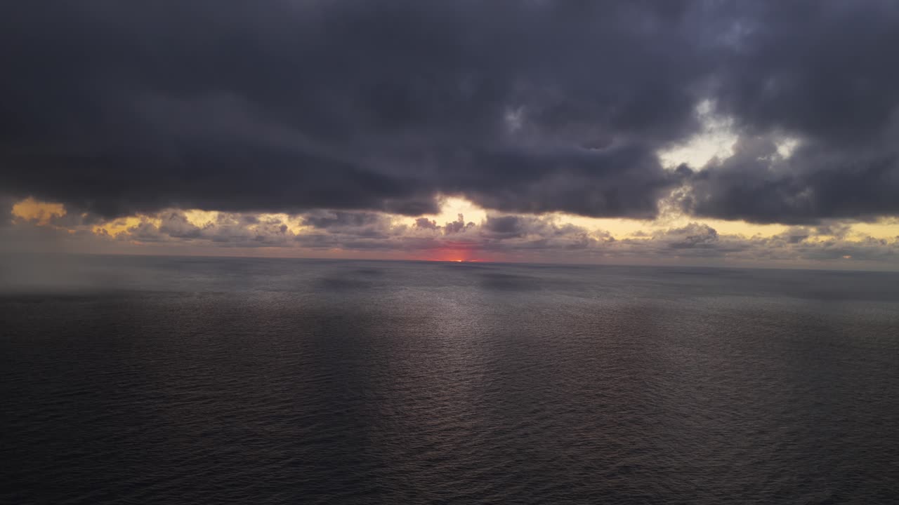 Sunset over the ocean at golden hour with silhouettes and rugged coastline.
