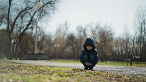 a close-up of a young boy in a shiny black jacket and head warmer, crossed his hands with a curious expression, the background is blurred, with soft natural light