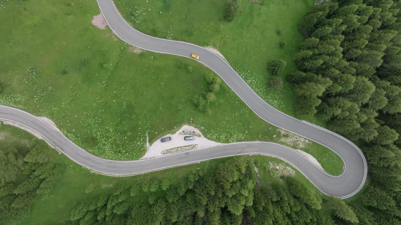 una vista aérea muestra dos coches atravesando las carreteras sinuosas cerca del paso de selva en las montañas dolomitas, trentino, tirol del sur, italia