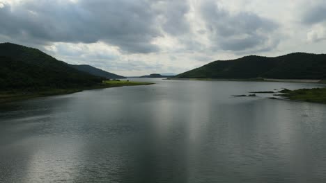 Aerial-footage-over-a-lake-revealing-a-wide-view,-a-bird-in-front-of-the-camera,-lovely-horizon-and-rainclouds,-Muak-Klek,-Saraburi,-Thailand