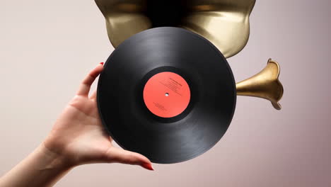 a hand holding a vinyl record in front of a brass instrument