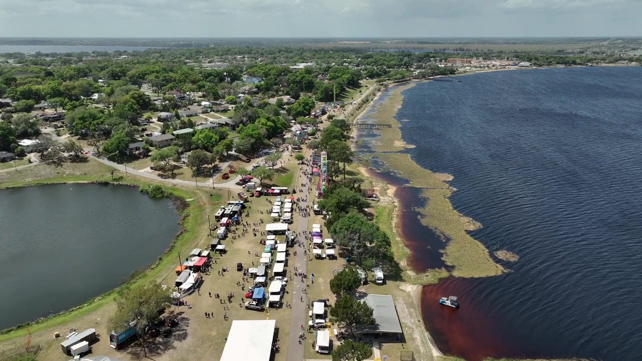 Riprese aeree ad alta quota di Pig on the Pond, un amato festival della Florida centrale a Clermont, con file di venditori, attrazioni fieristiche e una folla vivace vicino all'acqua.