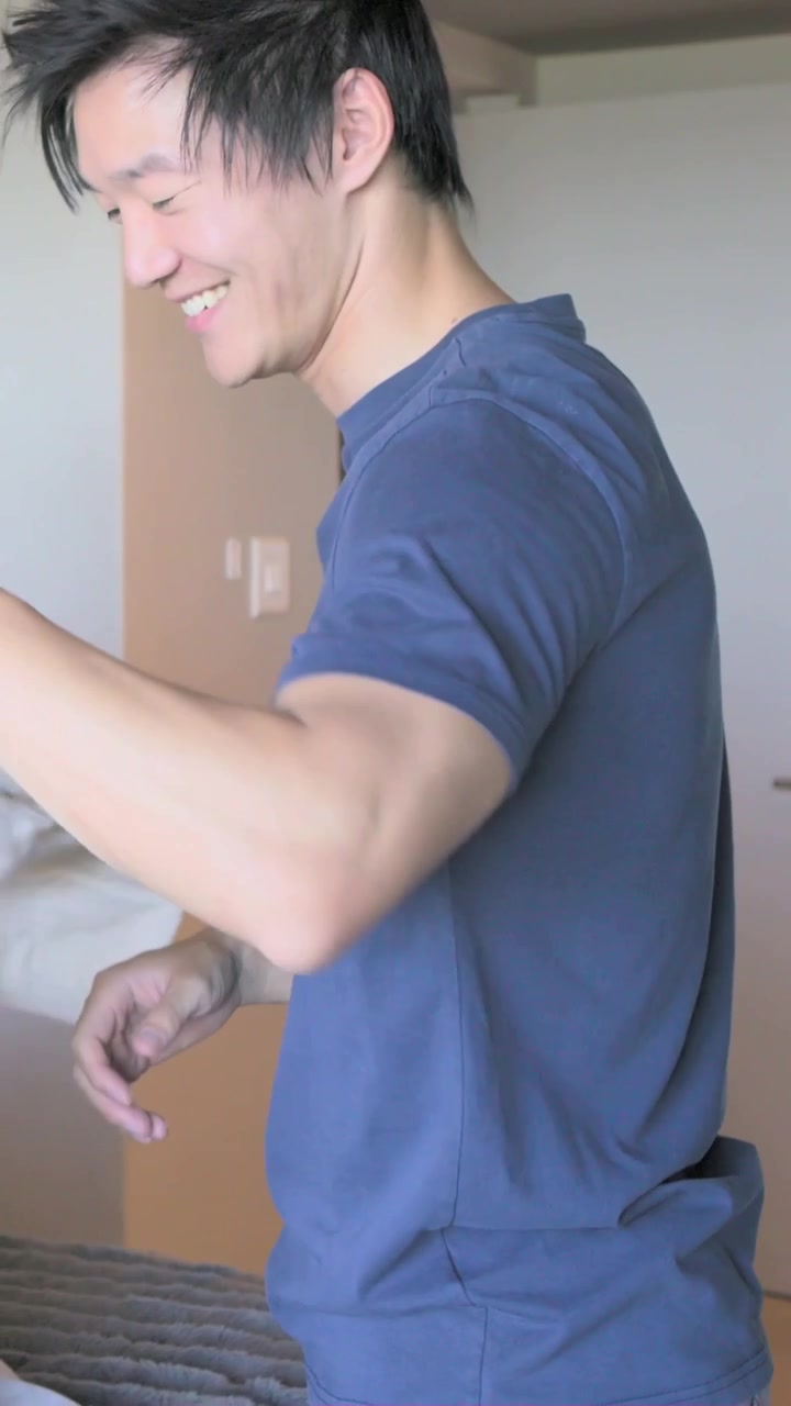 縦型動画：友人からリネンを受け取り、紺色のTシャツを着た男性がそれらをベッドに広げて整える。