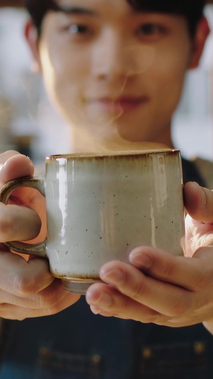 Video verticale: Dopo la mescita, cameriere in un caffè con grembiule di jeans che spinge una tazza di ceramica per servire.