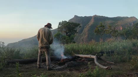 a western tourist warms himself by a fire on top of a mountain in east africa while camping