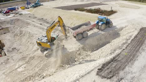 Aerial-drone-rotating-shot-over-JCB-digging-and-putting-soil-on-a-tractor-at-a-construction-site-on-a-sunny-day