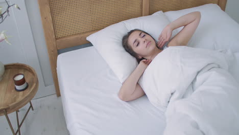 young woman wakes up in bed in the morning smiling raises her hands