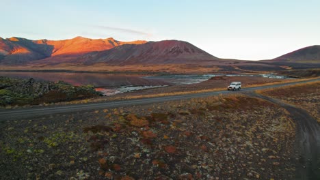 camioneta blanca conduciendo por la carretera del círculo dorado en islandia en un hermoso paisaje volcánico naranja rojo durante la puesta de sol