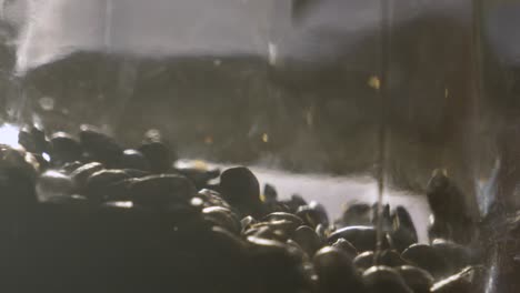 roasted coffee beans being dropped into glass jar in bright sunlight. ready to grind and make into caffeine hot drink beverage 4k.