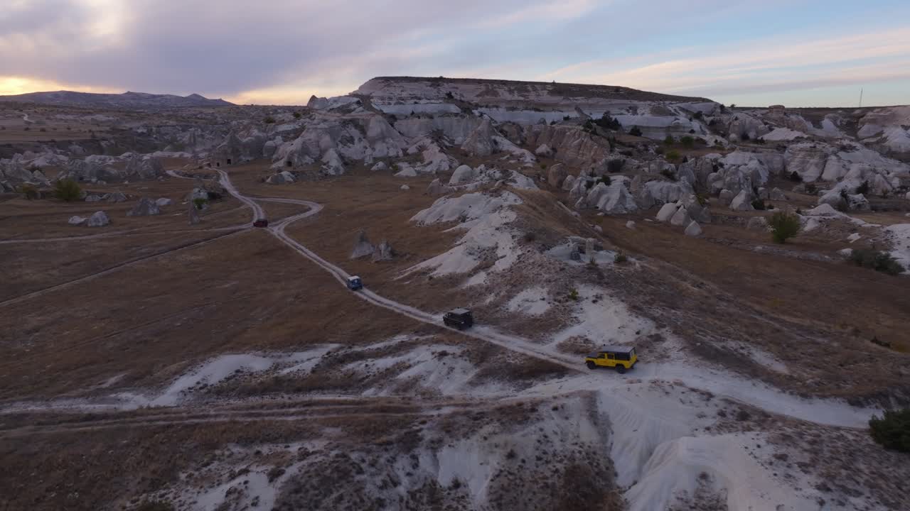 Veicoli fuoristrada che attraversano una valle rocciosa scolpita alla luce del tramonto