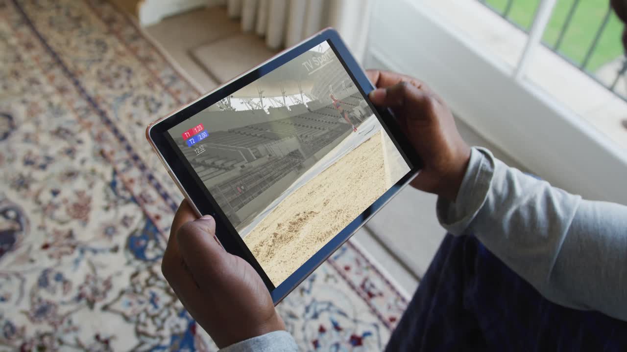 compuesto de un hombre sentado en casa, viendo el evento de salto de longitud de atletismo en la tableta
