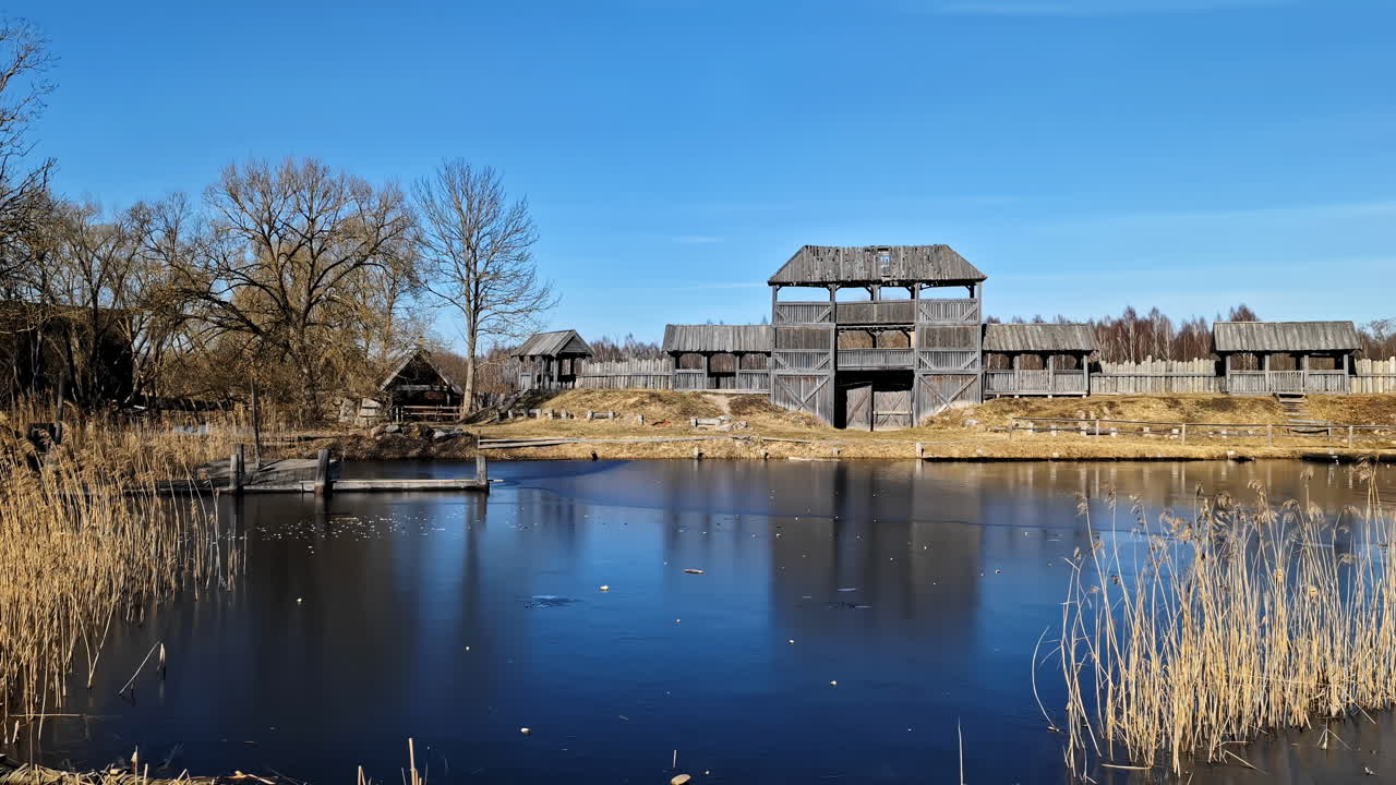 Wooden walls with tower and observation decks by a calm lake with reflections in the water, under a clear sky, in a natural setting