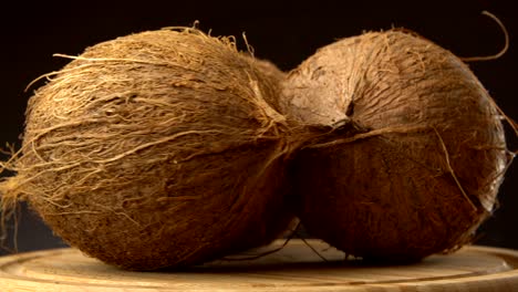 tres cocos tropicales maduros girando en una mesa de madera contra un fondo negro.