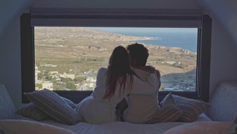 young millenial female lover embraces boyfriend on romantic night overlooking the sea in luxury hotel room