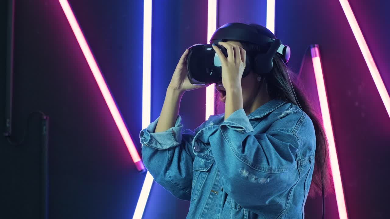 una giovane donna indossa un auricolare vr, si guarda intorno e si chiede come sia fantastico nella realtà virtuale. casco di realtà virtuale sullo sfondo di illuminazione a colori