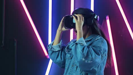 una mujer joven se pone un auricular vr, mira a su alrededor y se pregunta qué tan increíble es la realidad virtual. casco de realidad virtual en fondo de iluminación de color