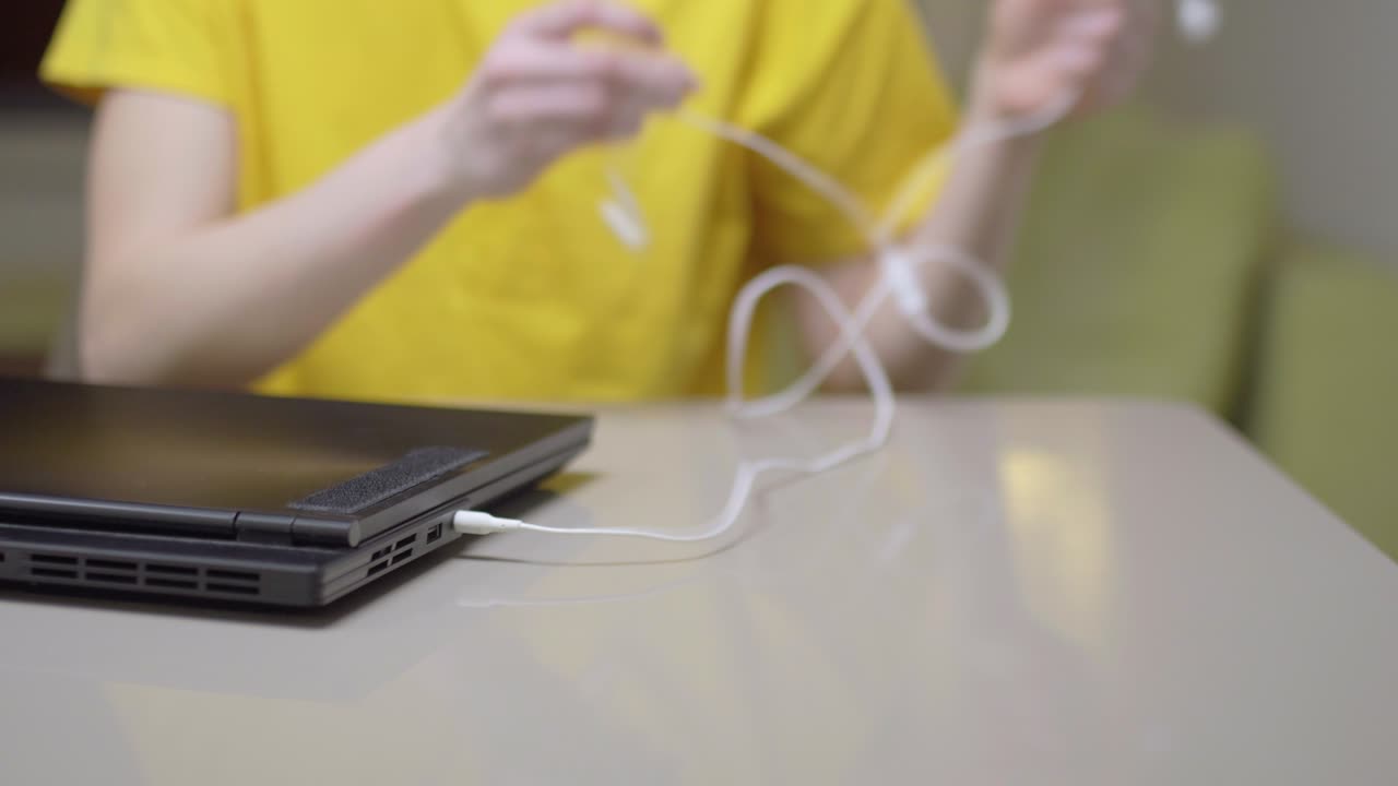 Young girl in yellow infront of a laptop computer. Plugging in earphones..