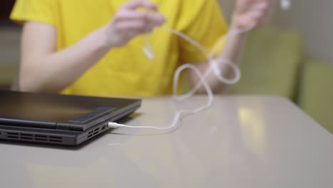 young girl in yellow infront of a laptop computer. plugging in earphones..
