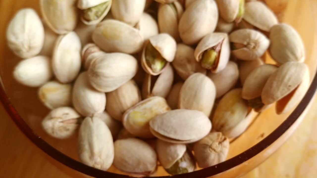 Glass bowl full of pistachio seeds on kitchen table from above, dolly