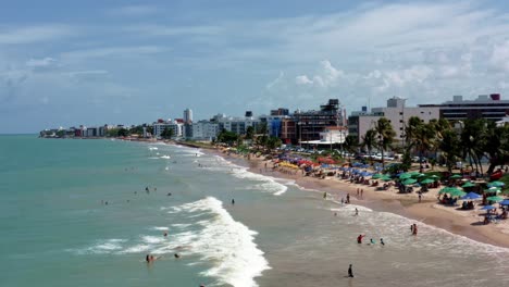 Dolly-out-aerial-shot-of-intermares-beach-in-Cabedelo,-Brazil-with-Brazilians-and-tourists-enjoying-the-ocean-near-the-costal-capital-of-Joao-Pessoa-in-the-state-of-Paraiba-on-a-warm-sunny-summer-day