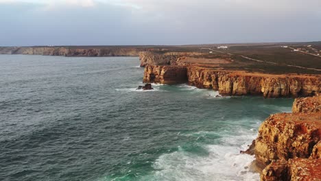 Erodierte-Rote-Meeresklippen-Von-Tonel-Beach-Im-Süden-Portugals,-Die-Von-Wellen-Bespritzt-Werden,-Luftüberführung-Zeigt-Aufnahme