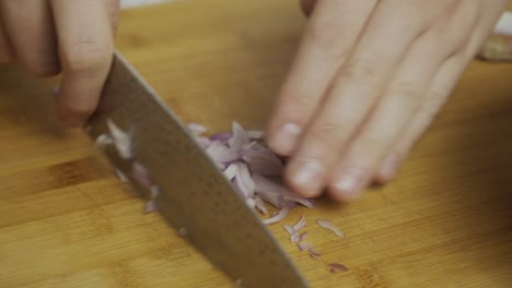 chef slices onion on wooden cut board