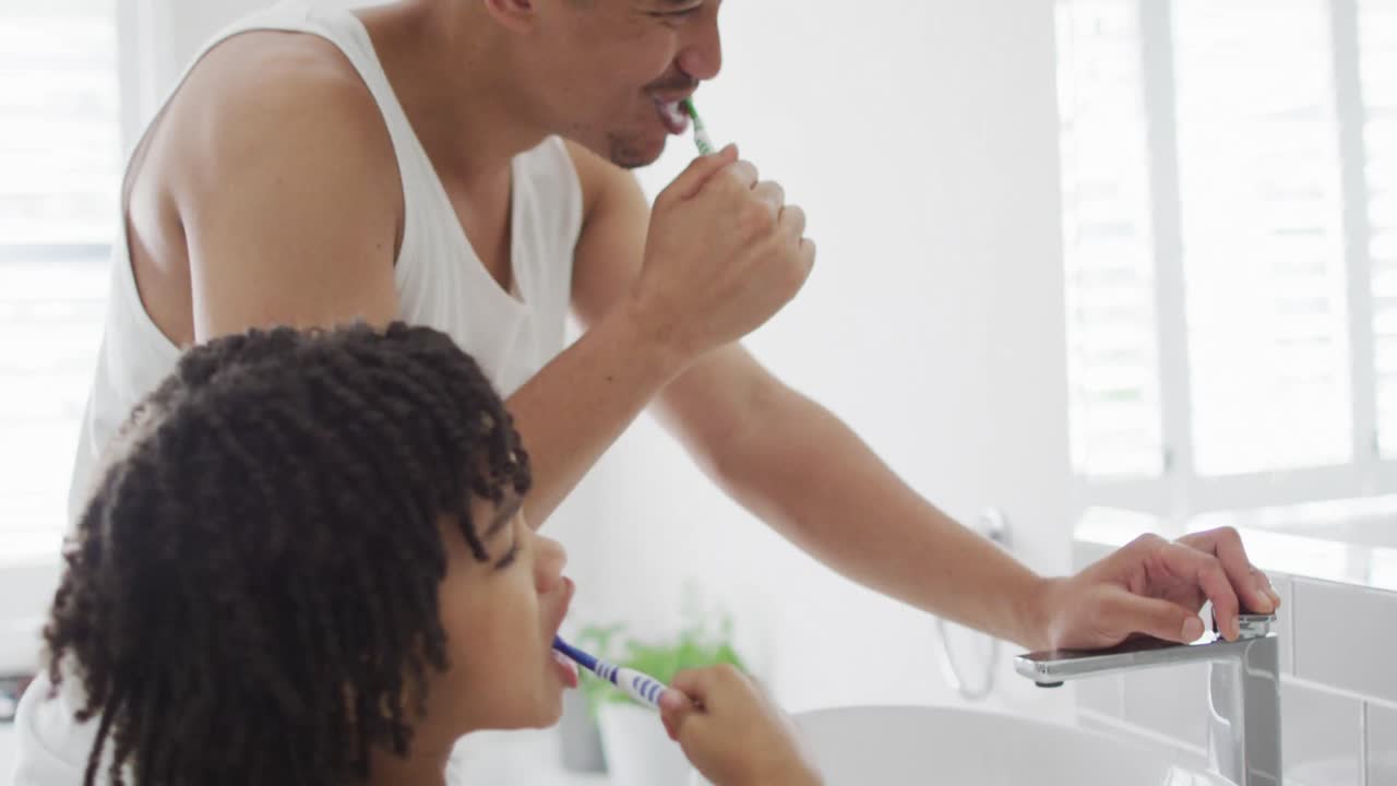 Happy biracial man and his son washing teeth in bathroom