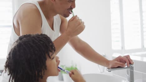 feliz hombre biracial y su hijo lavándose los dientes en el baño