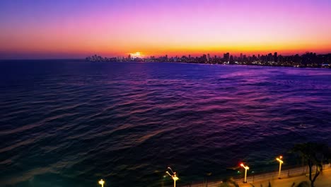 stunning sunset paints the city skyline with vibrant hues of orange, yellow, and purple over the tranquil ocean