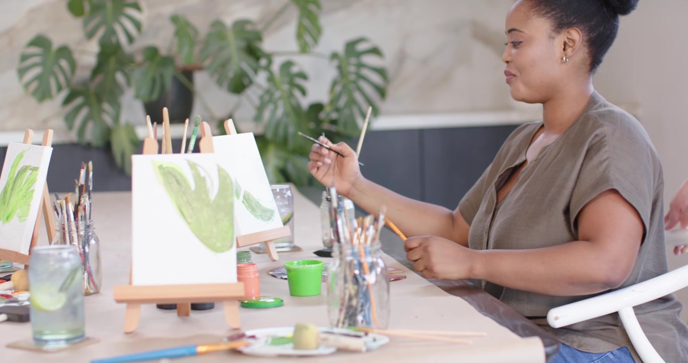 Female friends, woman entering giving feedback while seated painter painting green canvases