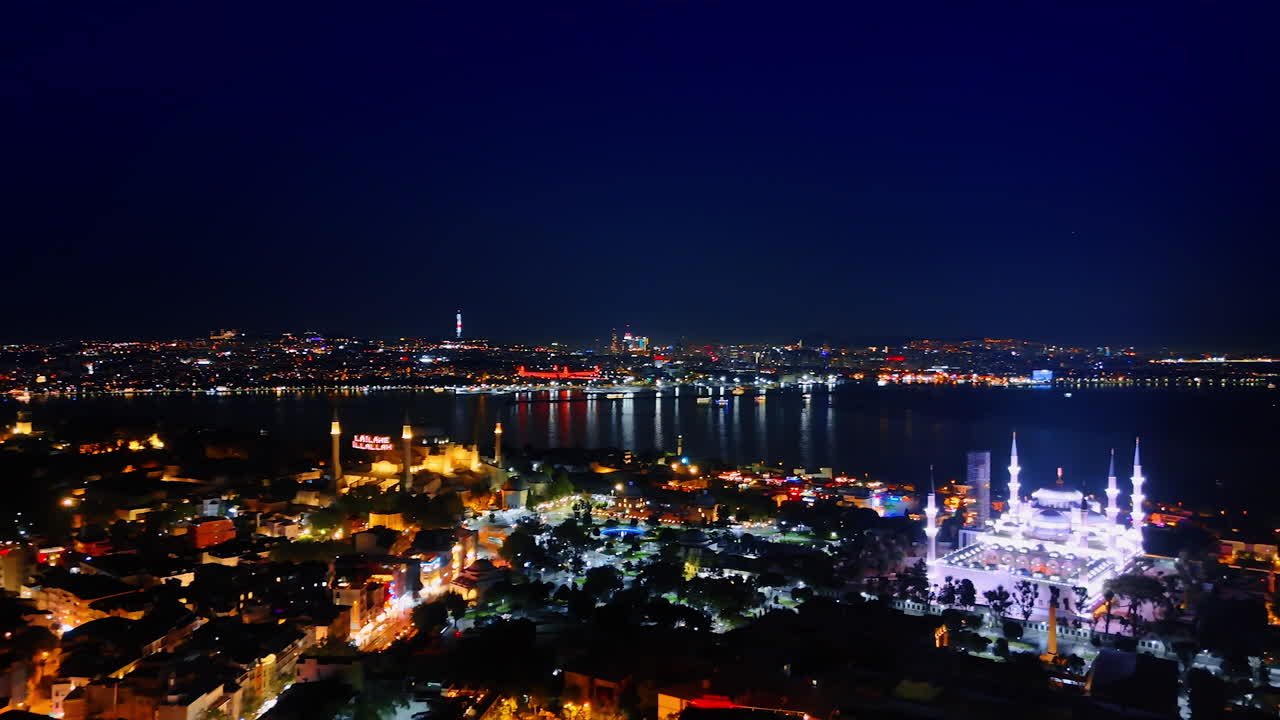 Light of the night city reflects in the dark waterscape. Aerial view of Istanbul, Turkey. Fantastically illuminated mosques in the cityscape