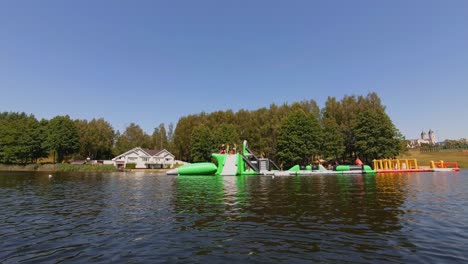 a floating inflatable water park on a calm lake with people enjoying the attractions