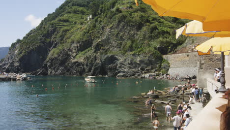 tourists on holiday at the rocky shore of porto di vernazza in cinque terre, italy. static shot