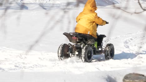 boy driving mini atv in snow on bright winter day in lapland