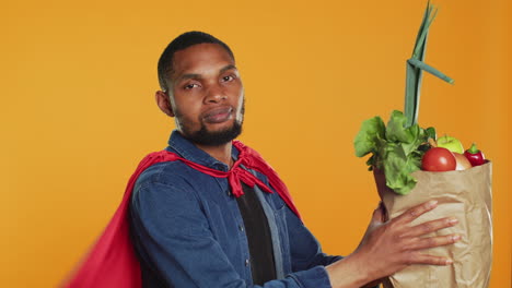 young adult acting as a superhero with a red cape presenting homegrown produce