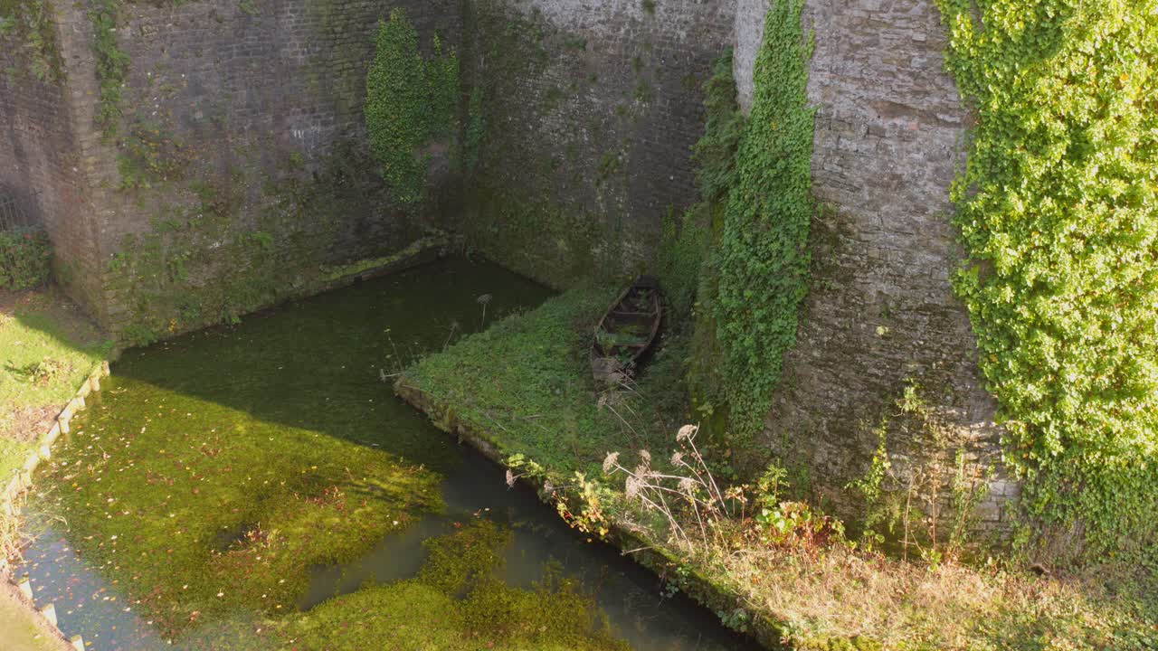 Static aerial view of an old boat covered in vegetation inside the moat of historic Boulogne castle