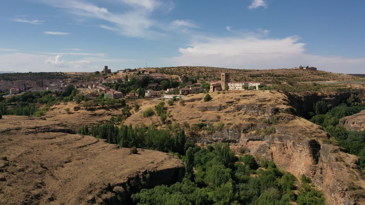 vuelo lateral con un dron observando el curso de un cañón y descubriendo una hermosa ciudad con su torre y sus prados secos porque es verano con un cielo azul en segovia españa