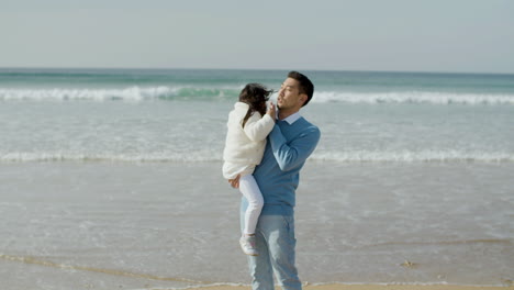 Fürsorglicher-Japanischer-Vater,-Der-Seine-Kleine-Tochter-An-Einem-Sonnigen-Tag-Am-Strand-In-Den-Armen-Hält