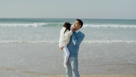 caring japanese father holding his little daughter in his arms at the beach on a sunny day