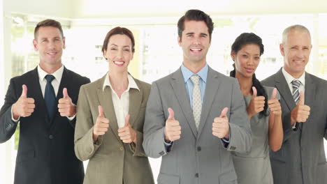 smiling business people looking at camera gesturing thumbs up