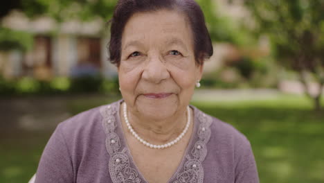 slow-motion-portrait-of-beautiful-elegant-elderly-woman-looking-at-camera-wearing-pearl-necklace-in-garden-background