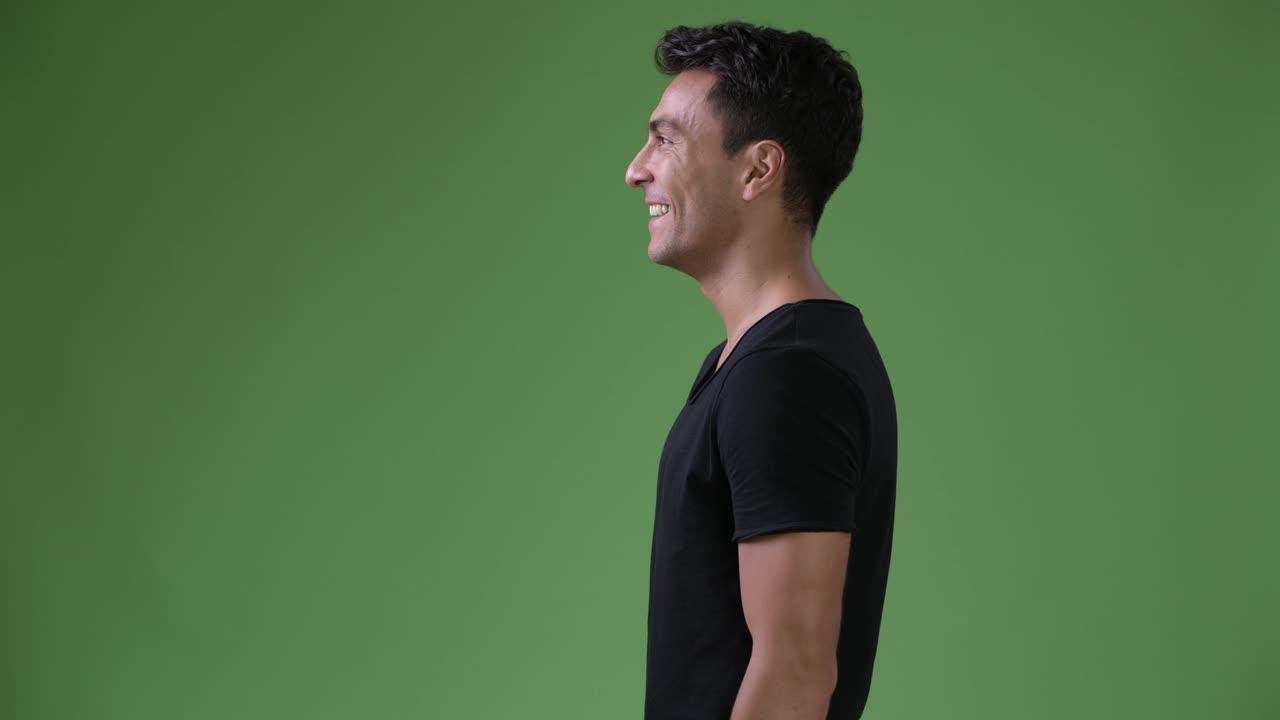 Young handsome Hispanic man against green background