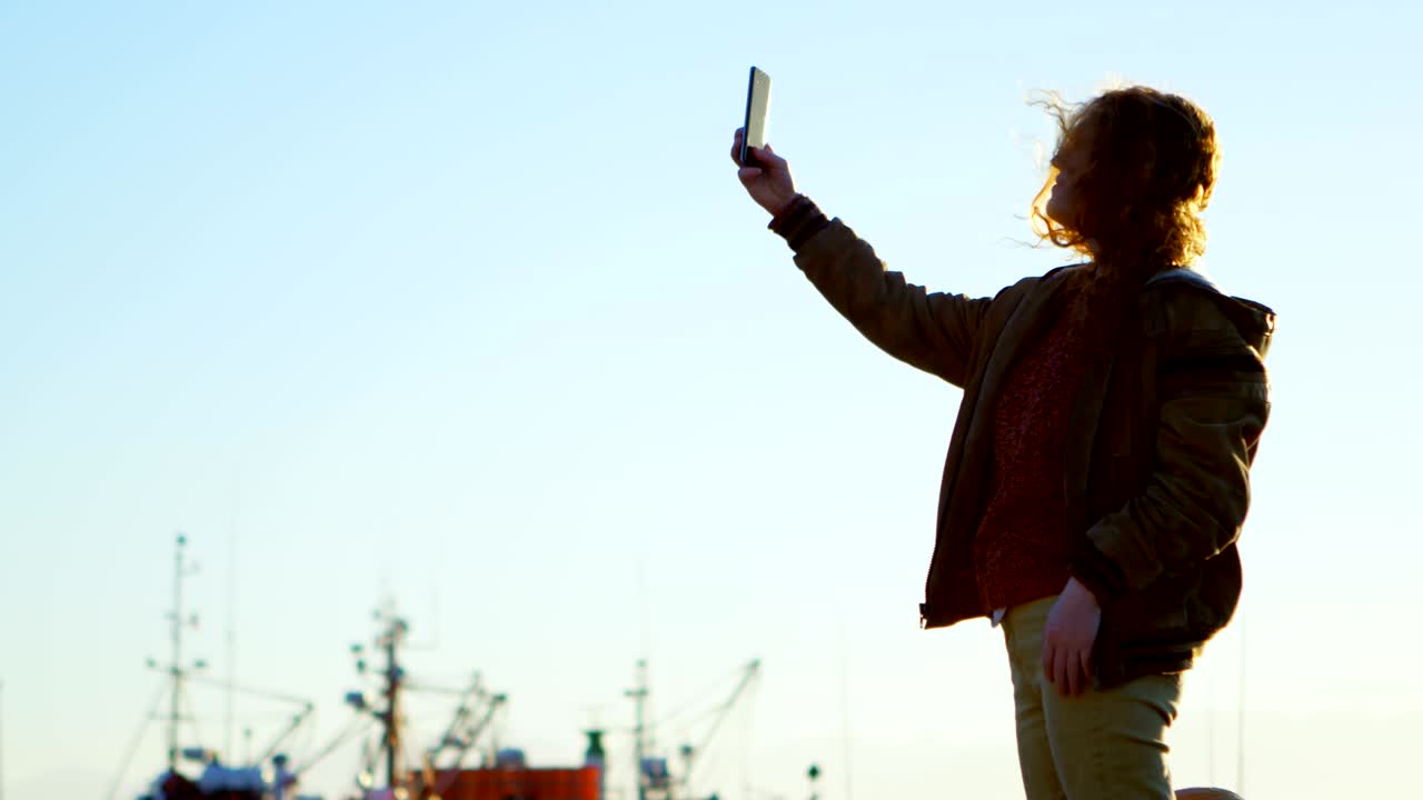 Donna che si scatta un selfie con lo smartphone al molo 4K