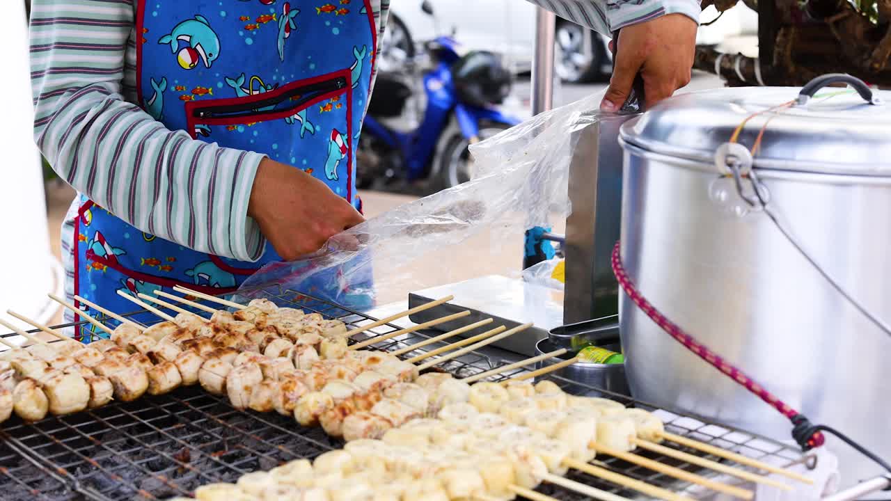 A street vendor grills bananas on skewers at a bustling Phuket market, showcasing vibrant colors and lively atmosphere