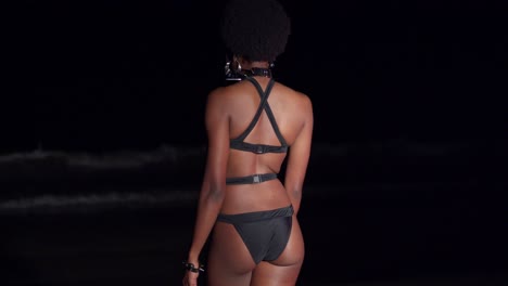 una mujer negra sexy sale a las olas del océano por la noche en bikini negro