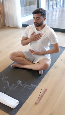 vertical video of biracial man doing yoga and meditating at home, slow motion