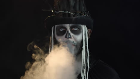 frightening man in creepy skeleton halloween cosplay exhaling cigarette smoke from his mouth