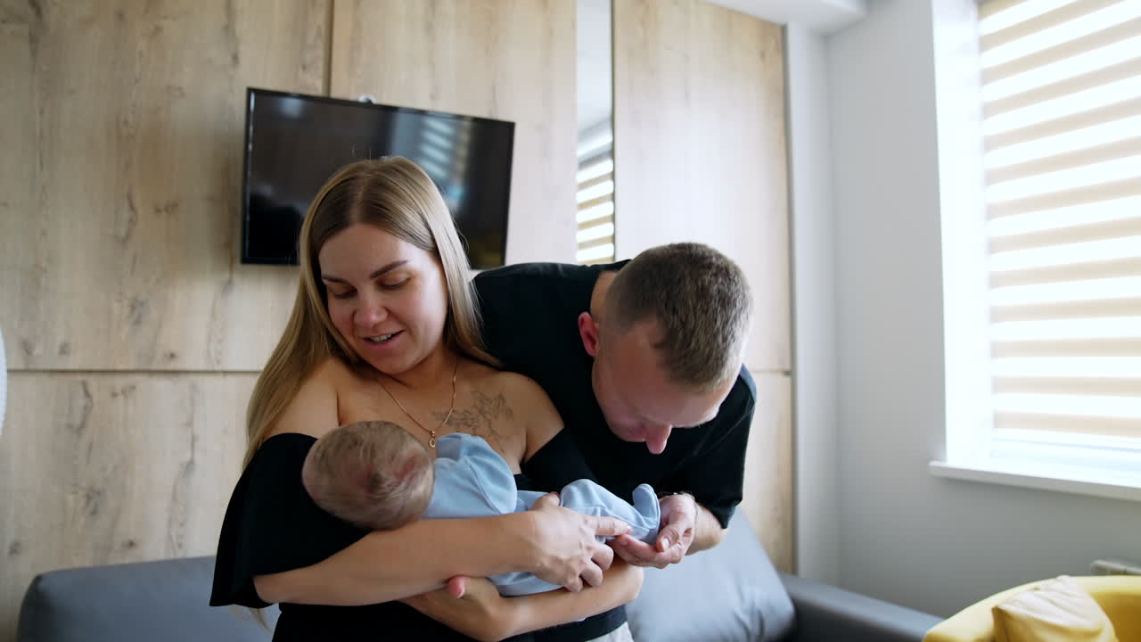 First time parents with their newborn in hospital. Happy couple look at child with love and then mom gives a baby to dad.