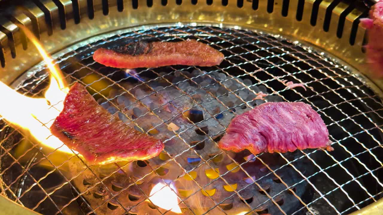 Ripresa ravvicinata dall'alto di carne di Wagyu cruda che cuoce su fiamme vive su una griglia a carbone